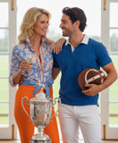 Women wearing a orange blue blouse with a polo player and champagne in her hand.