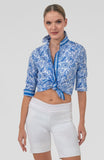 Woman wearing a blue patterned top and white shorts on a light gray background